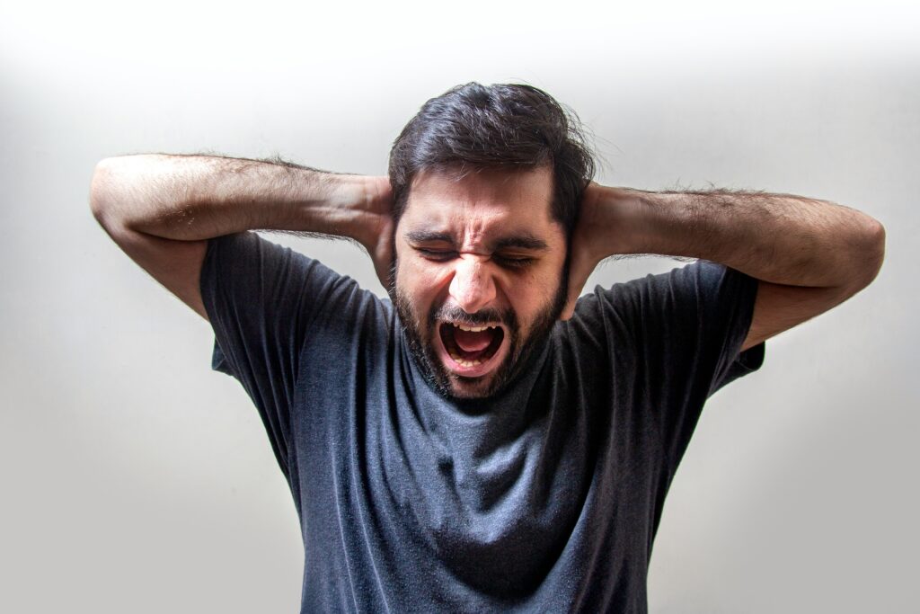 An image representing overstimulation. A photo of a man screaming with his hands over his ears.