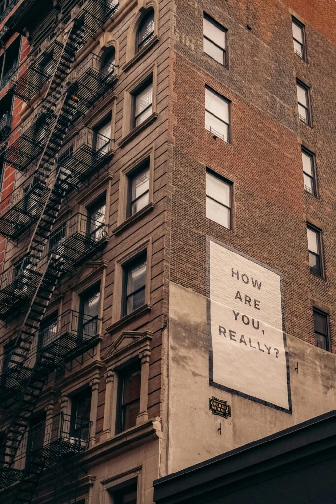 A block of apartments building with a sign with a therapy quote saying 'how are you really?'