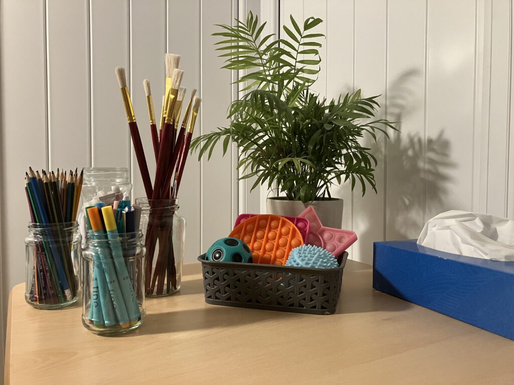 Creative therapy tools including paintbrushes, colouring pens, and fidget toys arranged on a table in the therapy room of a neurodivergent therapist in Stirling.