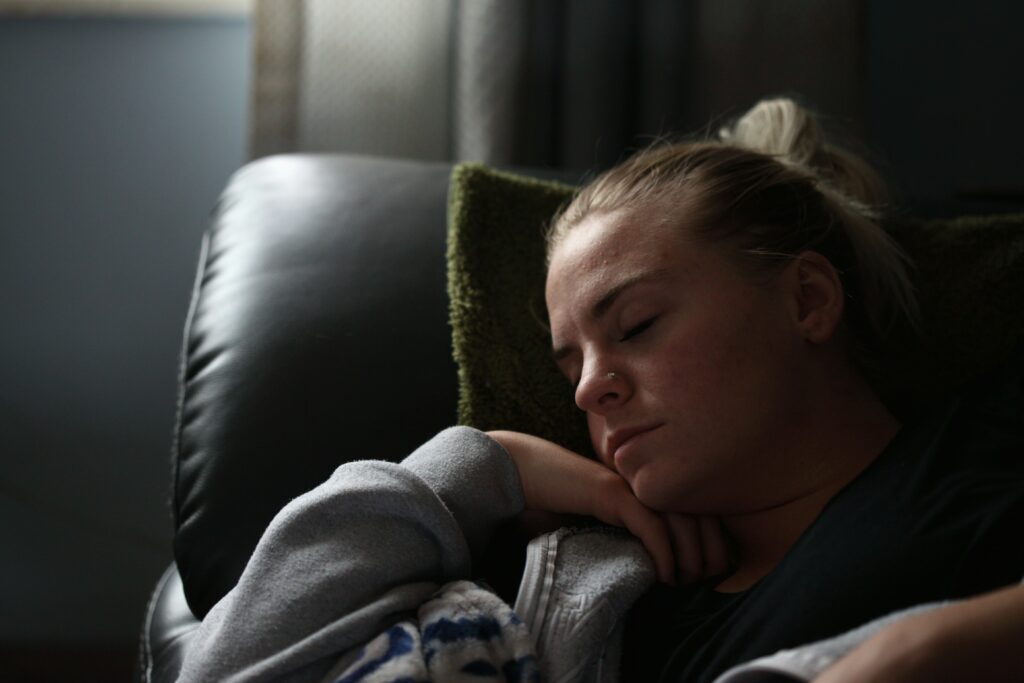 An image representing rest as a way to manage overstimulation. A photo of a person in a grey hoodie lying down with their eyes closed on a black sofa.